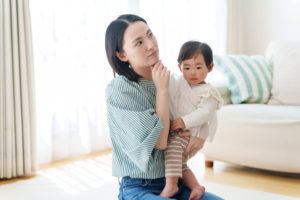 子供を抱っこしながら考える女性